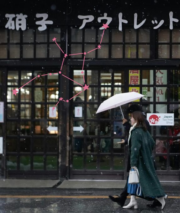 Two women under an umbrella walking past a Tokyo storefront in snow